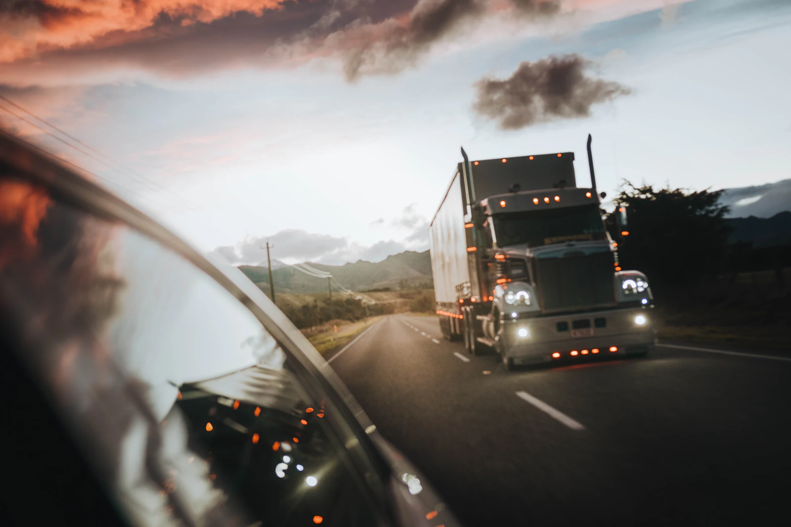 Semi truck approaching on a two-lane highway, seen past a car's side mirror