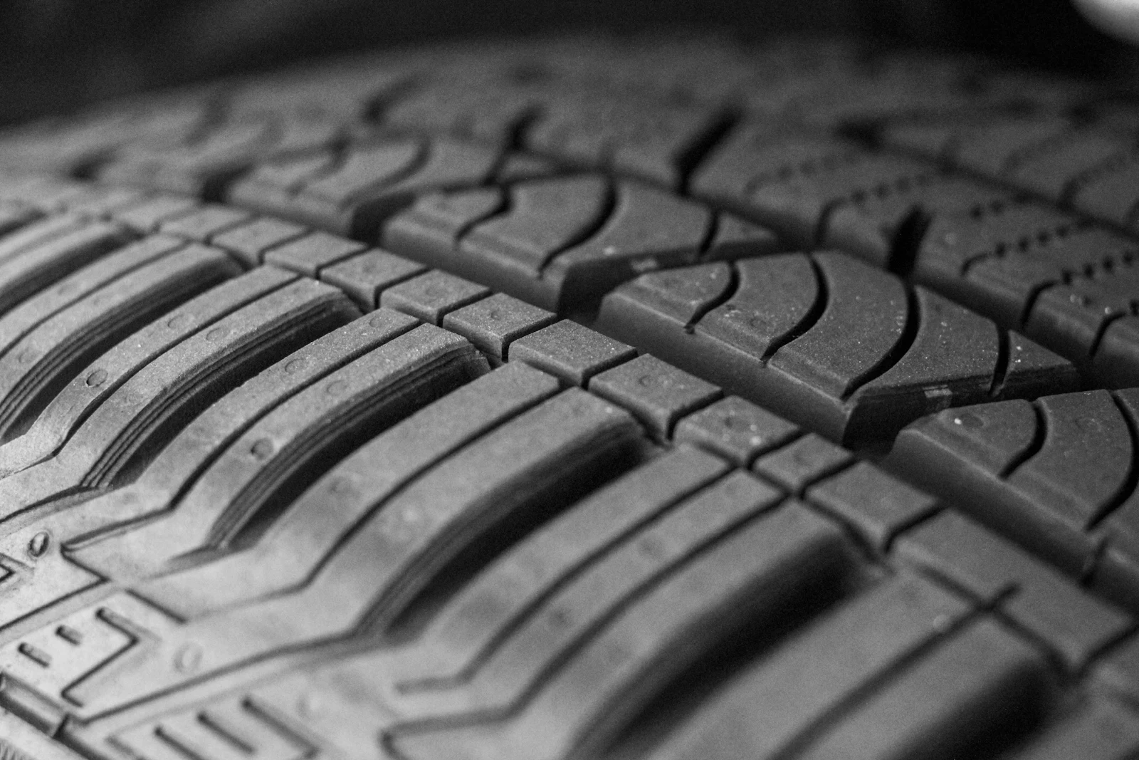 Black-and-white close-up of a passenger tire tread with ribs, blocks, and sipes